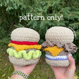 Könnte beinhalten: Zwei gehäkelte Hamburger-Amigurumi-Spielzeuge. Eines ist ein klassischer Hamburger mit Salat, Tomate, Käse und einem Sesambrötchen. Das andere ist ein Cheeseburger mit einem braunen Patty, Käse und einem lila Brötchen. Der Text "pattern only!" ist oben im Bild sichtbar.