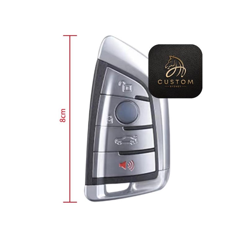 May include: A silver car key fob with five buttons, including a lock, unlock, trunk, and panic button. The key fob is 8 cm long.