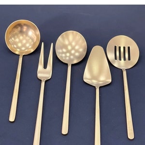 May include: A set of six gold-toned kitchen utensils, including a ladle, a slotted spoon, a serving spoon, a cake server, a fork, and a slotted spoon.