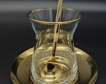 May include: A gold-rimmed glass teacup with a gold spoon on a gold saucer.