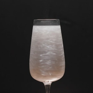 Puede incluir: Una copa de champán llena de un líquido rosa brillante e iridiscente. El líquido se arremolina y crea un efecto fascinante.