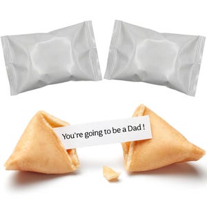 Pu&ograve; includere: Due biscotti della fortuna, uno rotto, con un messaggio che dice "You're going to be a Dad!". Due pacchetti bianchi sigillati sullo sfondo. I biscotti sono marrone dorato.