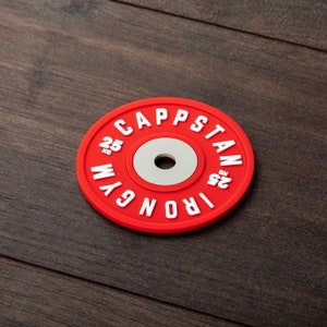 Pode incluir: Placa de peso vermelha com letras brancas que dizem "IRON GYM CAPSTAN 25 LB".