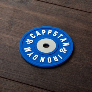 Pode incluir: Placa de peso azul com letras brancas que dizem "IRON 20 KG" e "CAPSTAN 20 KG" ao redor da borda.