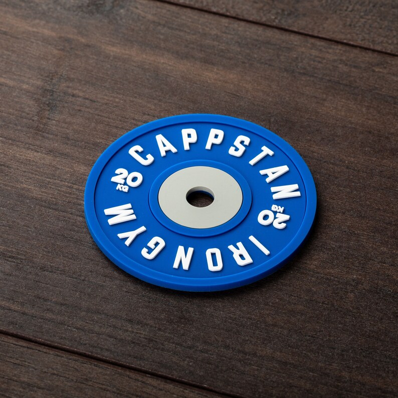 Pode incluir: Placa de peso azul com letras brancas que dizem "IRON 20 KG" e "CAPSTAN 20 KG" ao redor da borda.