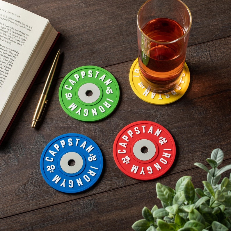 Pode incluir: Quatro  tapetes redondos com um design de placa de peso. Os tapetes s&atilde;o verde, azul, vermelho e amarelo. Cada tapete tem o texto "CAPPSTAN IRON GYM" impresso nele.