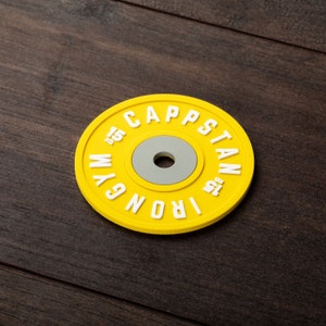 Pode incluir: Placa de peso amarela com o texto "IRON GYM CAPSTAN 1.25 KG" em letras brancas.