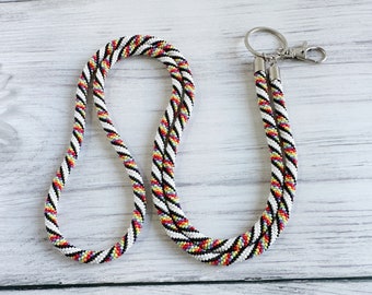 Op de afbeelding: Een wit, zwart, rood, geel en paars kralenkoord met een zilveren draaibare sluiting.