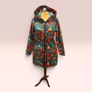 May include: A long-sleeved hooded jacket featuring a vibrant, multicoloured paisley and floral pattern on a dark teal background. The jacket includes a full-length black front zip, a drawstring waist with black cords, and two front pockets.
