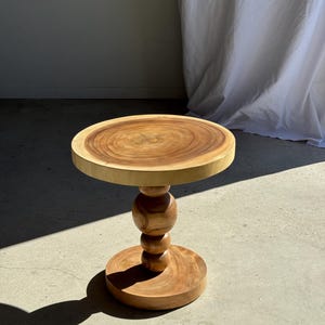 Op de afbeelding: Een kleine, ronde houten bijzettafel met een natuurlijke houtnerf afwerking. De tafel heeft een cirkelvormig blad, een gedraaide centrale kolom en een ronde voet. De tafel is ongeveer 51 cm hoog.