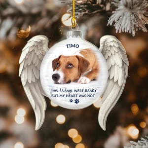May include: A clear glass Christmas ornament with a dog's portrait, angel wings, and the name "Timo." The ornament has the text "Your Wings Were Ready But My Heart Was Not" and paw prints. A gold string is attached for hanging.