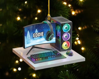 May include: A gaming PC Christmas ornament featuring a curved monitor displaying "EDDIE" over a winter scene. Includes a keyboard, mouse, and headset. The PC case has colorful LED fans. The ornament hangs from a gold string.