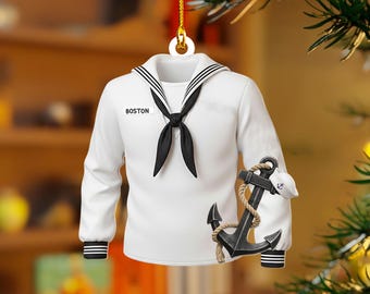 May include: A white sailor uniform Christmas ornament with black accents, including a black tie, collar stripes, and sleeve stripes. The word "BOSTON" is printed on the chest. An anchor and sailor hat are attached.