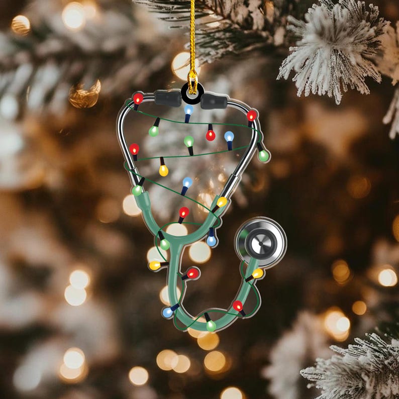 May include: A Christmas tree ornament shaped like a stethoscope, with a green body and silver tubing. The ornament is decorated with a string of colorful Christmas lights. The background is a blurred image of a Christmas tree.