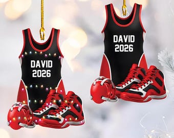 May include: Two hanging ornaments shaped like wrestling singlets, each featuring the name DAVID and the year 2026 in white text. The black and red singlets are paired with red wrestling headgear and red and black wrestling shoes.