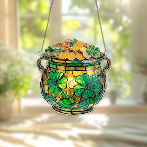 May include: Stained glass pot of gold with a green and gold color scheme. The pot is decorated with shamrocks and filled with gold coins. The pot is hanging from a chain, perfect for St. Patrick's Day.