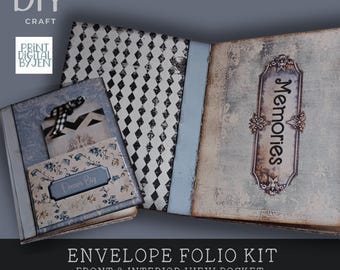 May include: An open envelope folio kit with a vintage aesthetic. The kit includes a journal with a diamond pattern, a pocket with a floral design, and a tag with a black and white pattern. The text "Memories" is visible on the journal. The text "Dream Big" is visible on the pocket.