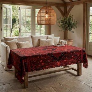 May include: A rectangular tablecloth featuring a deep red and black ornate pattern with a scalloped edge. The fabric drapes over a wooden table, displaying a central geometric motif and intricate border details across the entire surface area.