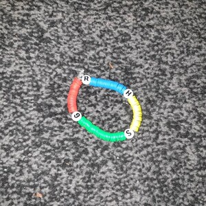 May include: A colourful bracelet made of small plastic rings with letters and numbers. The bracelet is red, yellow, blue, and green.