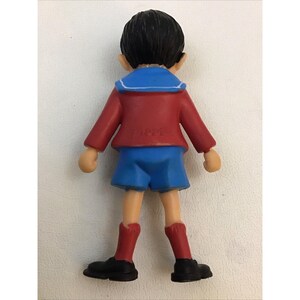 Puede incluir: Una figura de pl&aacute;stico de un ni&ntilde;o que lleva una camisa de marinero roja y azul, pantalones cortos azules y zapatos negros. La figura mide aproximadamente 15 cm de alto.