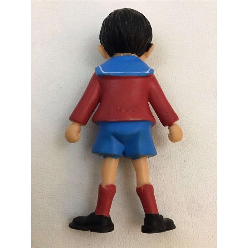 Puede incluir: Una figura de pl&aacute;stico de un ni&ntilde;o que lleva una camisa de marinero roja y azul, pantalones cortos azules y zapatos negros. La figura mide aproximadamente 15 cm de alto.