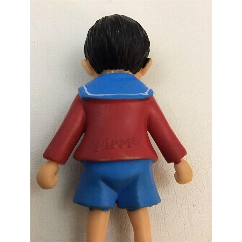 Puede incluir: Una figurita de pl&aacute;stico de un ni&ntilde;o con una camisa de marinero y pantalones cortos, de color rojo y azul. La figurita est&aacute; hecha de pl&aacute;stico y tiene una inscripci&oacute;n blanca en la parte posterior que dice "Pierre".