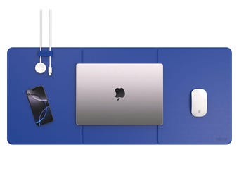 May include: A blue desk mat with a laptop, phone, mouse, and charging accessories. The laptop is silver with a black apple logo. The phone has a black screen. The mouse is white. The charging accessories are white.