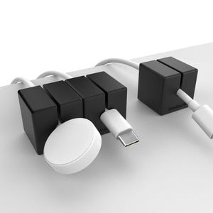 May include: Black cable organizers with four slots and one slot, holding various cables and a white charging puck.