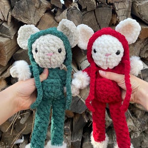 May include: Two handmade crochet bunny dolls. One is green, the other is red. Both have white faces, ears, and fluffy feet. The dolls are wearing hooded outfits and have pink noses and black eyes.