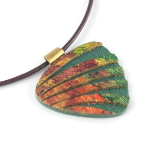 Puede incluir: Un collar con un colgante de patrón verde, naranja y amarillo con un cordón de cuero marrón.