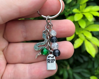 May include: A silver keyring with a snake charm, green bead, black and white beads, and a silver tombstone charm with the word "RIP" on it.