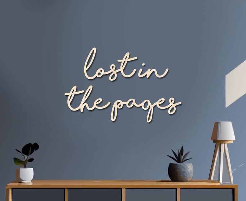 May include: Wooden wall art with the phrase "lost in the pages" in a cursive font. The text is light beige and mounted on a blue wall. A wooden table with plants and a lamp is below the text.