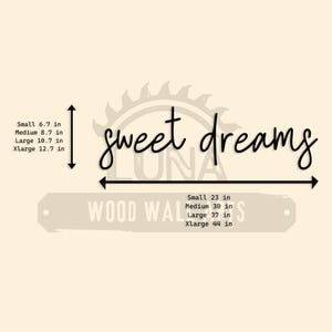 May include: A beige background with the words "sweet dreams" in black cursive script. Below, a rectangular sign reads "WOOD WALLS" with size measurements in inches: Small 23 in, Medium 30 in, Large 37 in, Xlarge 44 in.