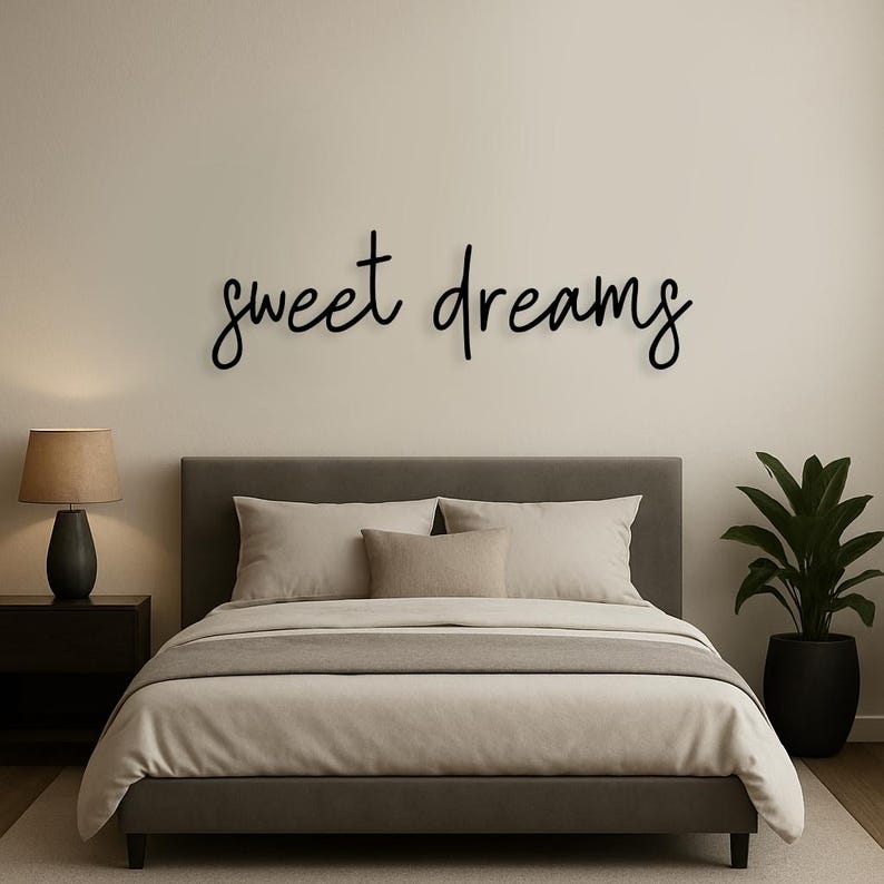 May include: A bedroom scene featuring a bed with neutral-toned bedding and pillows. Above the bed, the words "sweet dreams" are displayed in a cursive font. A lamp and a potted plant are also visible.