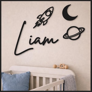 Peut inclure: Décoration murale en bois noir avec le nom "Liam" en écriture cursive, accompagnée d'une fusée, d'une lune et d'une planète. Idéale pour une chambre d'enfant, cette décoration sur le thème de l'espace ajoute une touche ludique.