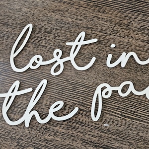 May include: White wooden cut-out letters spelling "lost in the past" in a cursive font. The letters are arranged on a dark brown wooden surface. The letters are a decorative element.