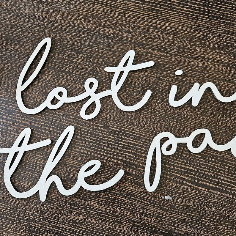 May include: White wooden cut-out letters spelling "lost in the past" in a cursive font. The letters are arranged on a dark brown wooden surface. The letters are a decorative element.