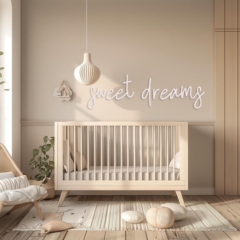 May include: A nursery scene with a light wood crib, a rug, and decorative pillows. The wall features the phrase "sweet dreams" in cursive. A hanging pendant light and a small shelf add to the room's decor. The overall color scheme is neutral.