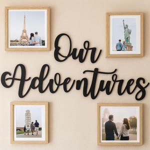 May include: A wall art display featuring four framed photographs and a black cursive sign that reads "Our Adventures." The photographs are of travel destinations, including the Eiffel Tower and the Statue of Liberty. The frames are light brown.