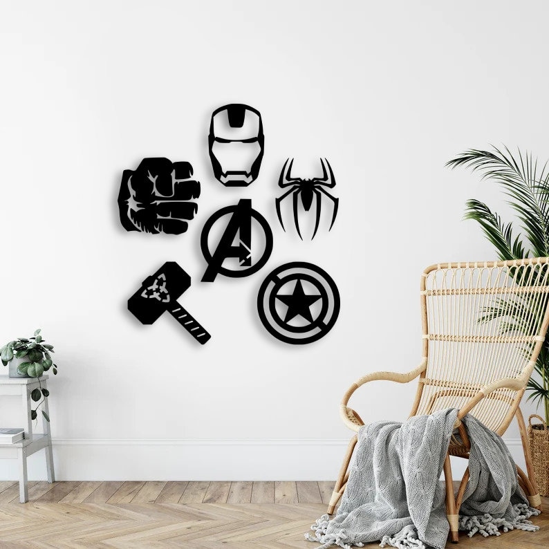 K&ouml;nnte beinhalten: Eine Ansammlung von sechs schwarzen Wanddekorationen, bestehend aus einer Superheldenmaske, einer geballten Faust, einem Spinnenemblem, dem Avengers-Logo, einem Hammer und einem runden Schild mit einem Stern in der Mitte, angeordnet an einer wei&szlig;en Wand.