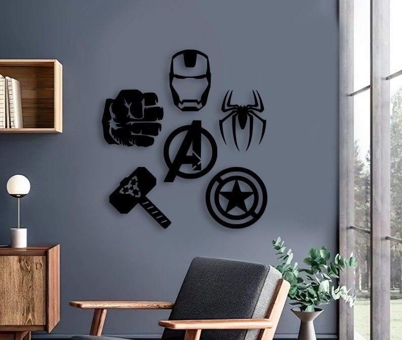 K&ouml;nnte beinhalten: Ein schwarzes Wandkunst-Set bestehend aus sechs verschiedenen Symbolen: einer geballten Faust, einem Iron-Man-Helm, einer Spinnensilhouette, dem Avengers-Logo, einem Hammer und einem runden Schild mit einem Stern in der Mitte, angeordnet an einer grauen Wand.