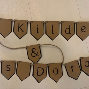 Könnte beinhalten: Ein braunes Papierbanner mit schwarzer Beschriftung, auf dem "Mr. Kildare & Mrs. Doran" steht.