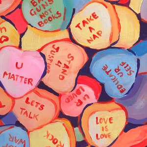 K&ouml;nnte beinhalten: Eine Sammlung herzf&ouml;rmiger S&uuml;&szlig;igkeiten mit verschiedenen Botschaften, die darauf gemalt sind, darunter "Ban Guns Not Books", "Take A Nap", "U Matter", "Lets Talk", "Love Is Love", "Rock U", "War Not Hug", "Up Loved", "Ur Self Educate" und "Just 4 Stand".
