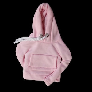 Könnte beinhalten: Ein rosa Kapuzenpullover mit einem weißen Kordelzug. Der Pullover hat eine Tasche auf der Vorderseite.