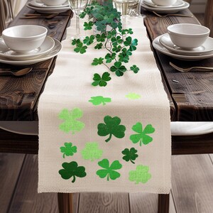 May include: A beige burlap table runner with a green shamrock pattern. The runner is decorated with green shamrocks of varying sizes.
