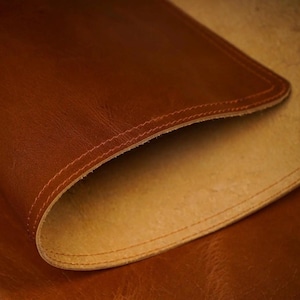 Close-up of a curled tan leather desk mat showing the underside