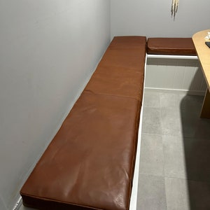May include: Two brown leather bench cushions in a corner nook. The cushions are attached to a white bench.