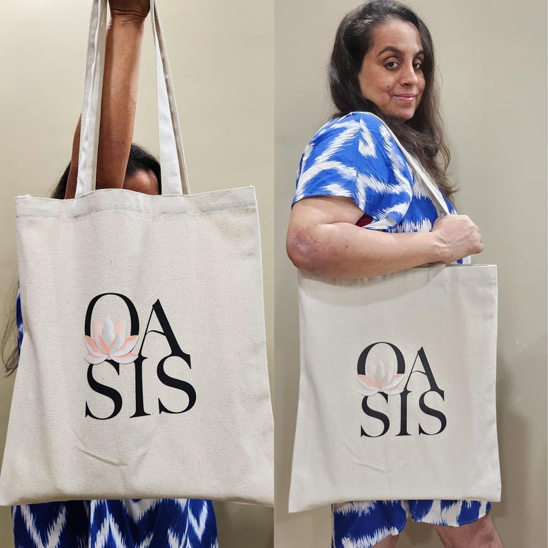 Puede incluir: Una bolsa de lona blanca con texto negro que dice "OASIS" y un gr&aacute;fico de flor rosa.