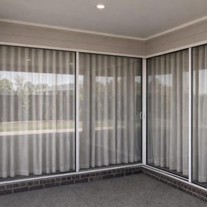 Puede incluir: Un espacio exterior moderno con grandes cortinas de color claro que cubren puertas correderas de vidrio. Las cortinas están plisadas verticalmente, brindando privacidad mientras permiten que la luz natural se filtre. El suelo es gris moteado y las paredes son de color beige claro.