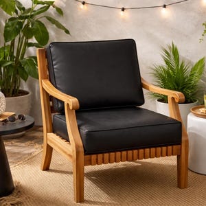 May include: Outdoor armchair with a natural wood frame and black cushion. The chair has a slatted seat and curved armrests. The setting includes plants, a side table, and string lights, creating a relaxing patio scene.